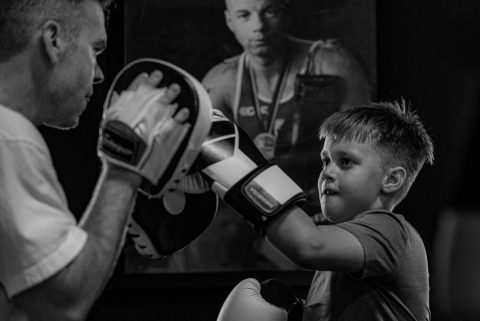 a child hits the boxing mitts during a kids class while smiling